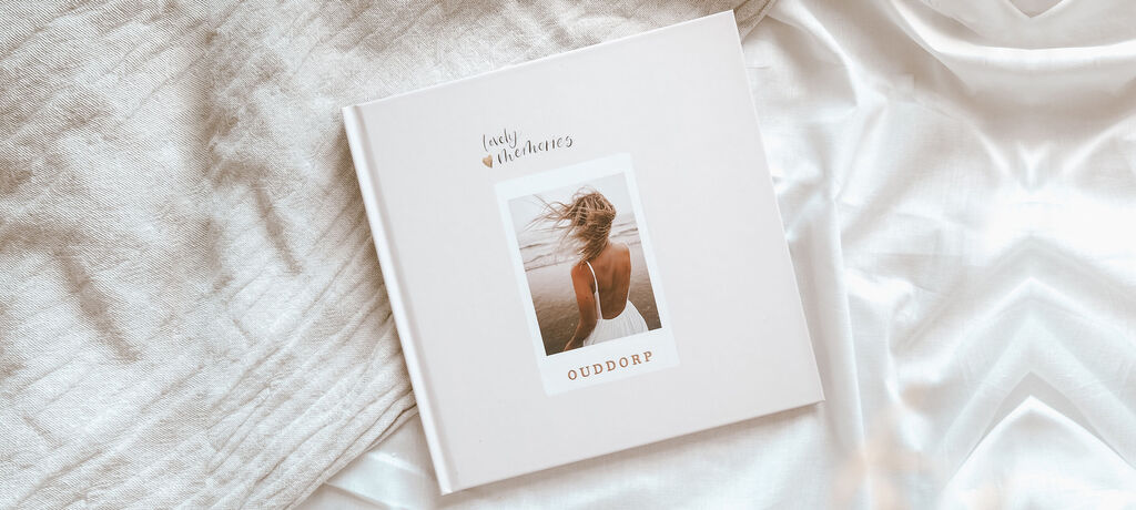 Ein geschlossenes CEWE Fotobuch liegt auf einem hellen, glatten Untergrund. Auf dem Cover ist ein Foto einer Person mit windgepeitschtem Haar am Strand zu sehen. Darüber steht ein herzlicher Text.