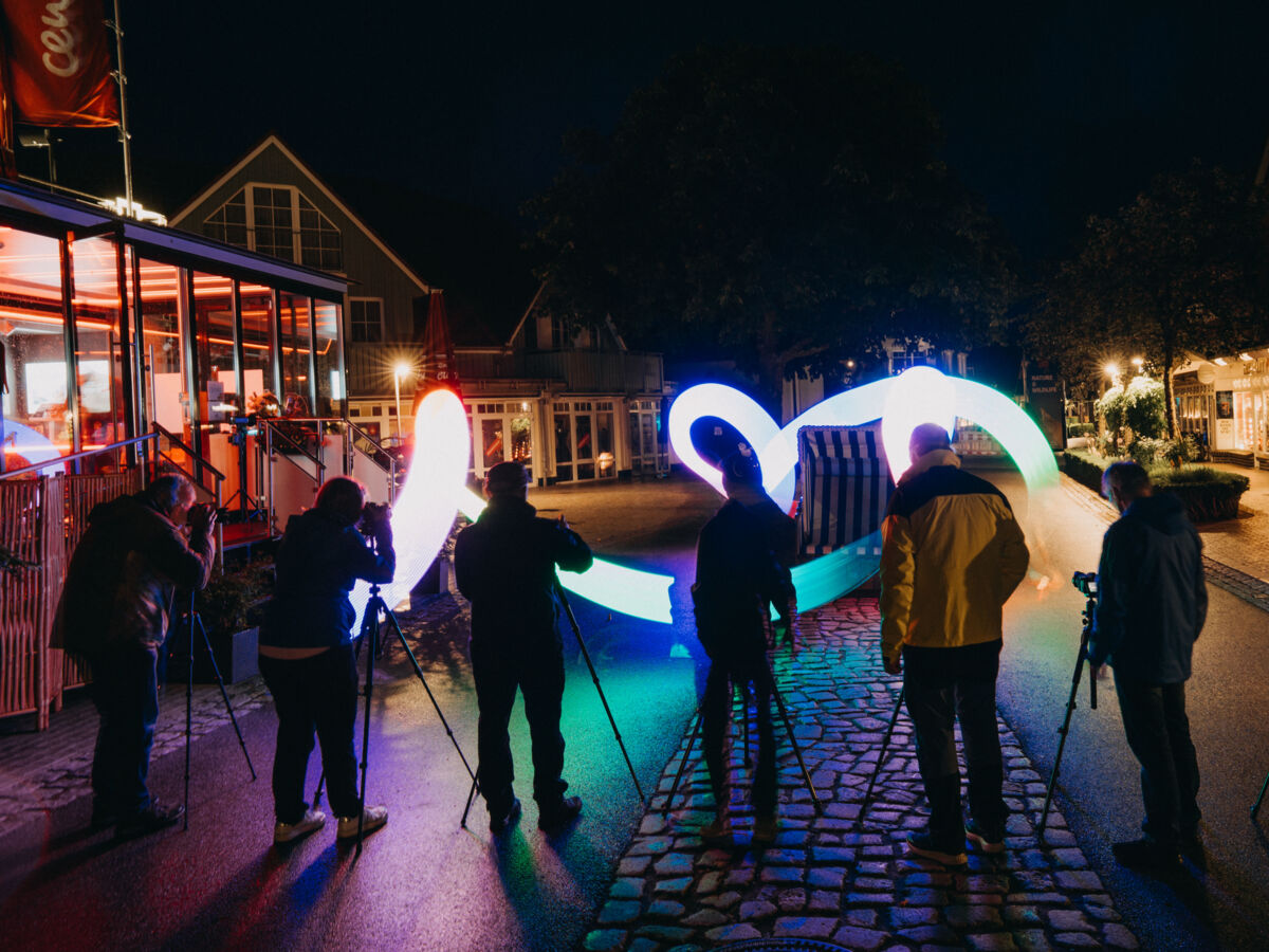 Mehrere Personen stehen im Dunkeln auf einer Straße und fotografieren mit Kameras auf Stativen einen Lichtstreifen.