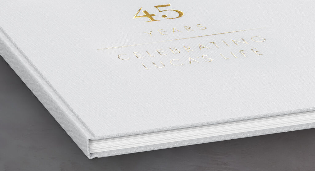 Ein weißes Fotobuch mit goldener Prägung für einen 45. Geburtstag gemeldet von CEWE FOTOBUCH.