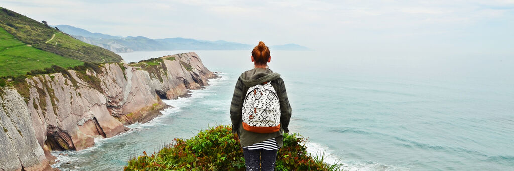 Junge Frau mit Rucksack blickt auf die Küste und das Meer.