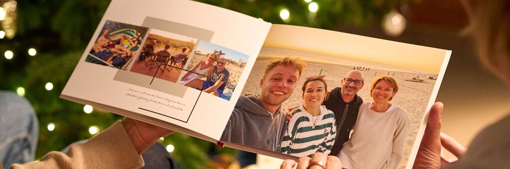 Eine Person hält ein geöffnete CEWE Fotobuch mit Fotos von Freunden und schönen Momenten am Strand.