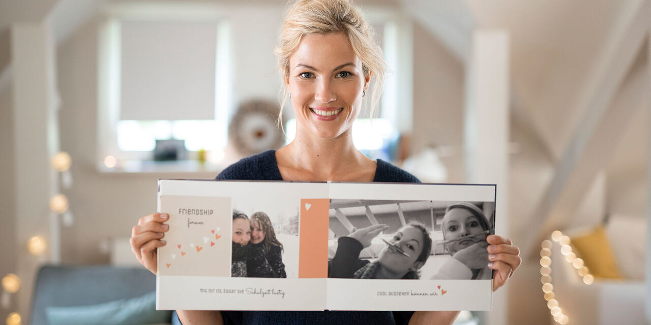 Eine Person zeigt stolz ein geöffnetes Fotobuch mit persönlichen Erinnerungen.