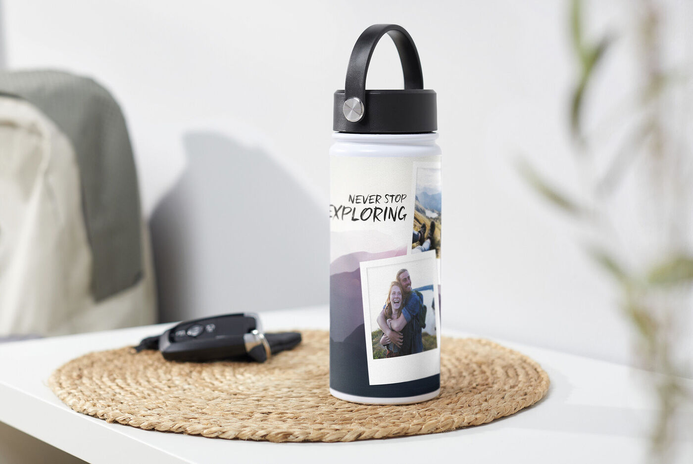 Eine personalisierte Trinkflasche mit Fotos und dem Text 'NEVER STOP EXPLORING' auf einem Tisch. Neben der Flasche liegt ein Autoschlüssel auf einem Platzdeckchen.