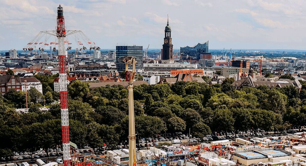 Jahrmarkt vor grünen Bäumen, im Hintergrund Hamburger Michel und Elbphilharmonie
