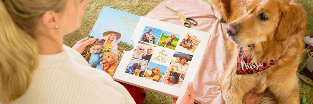 Person betrachtet mit Hund ein CEWE FOTOBUCH voller fröhlicher Fotos und gemeinsamer Erlebnisse.