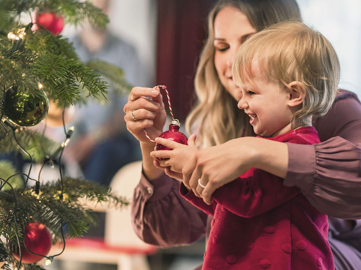 Ein Kind bringt einen roten Weihnachtsbaum-Ornament an den Baum.