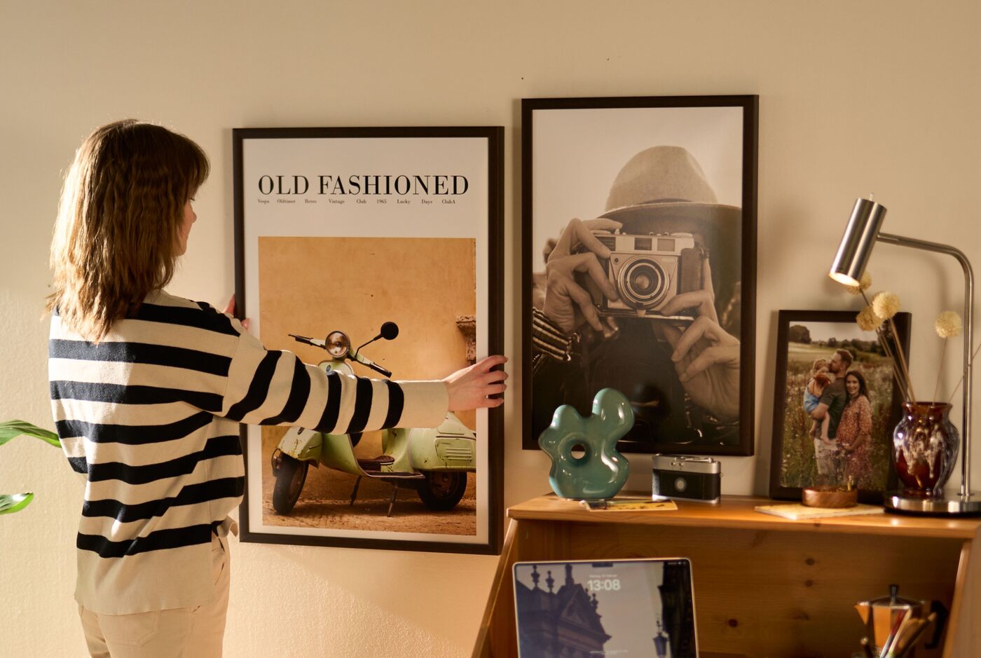 Ein Mädchen bringt ein Wandbild an. Daneben hängt bereits ein Wandbild, rechts neben den Bildern befindet sich ein brauner Holztisch