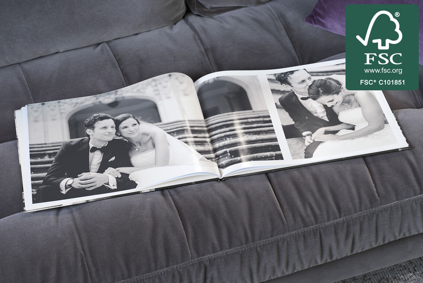 Ein aufgeschlagenes CEWE FOTOBUCH zeigt romantische Hochzeitsfotos auf einem Couchsofa in eleganter Umgebung