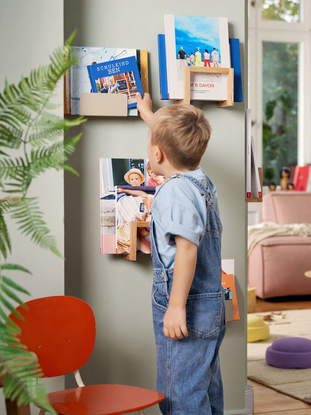 Ein kleiner Junge greift nach einem Buch an der Wand, umgeben von bunten Bildern