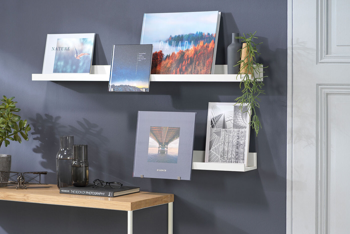 Regal mit mehreren CEWE Fotobüchern auf weißem Hintergrund, beinhaltet schöne Landschaftsbilder und kreative Designs