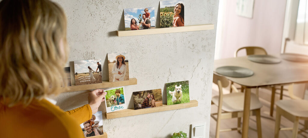 Eine Frau stellt ein Foto auf eine Fotoleiste an der Wand. Darin sind schon viele Fotos zu sehen.