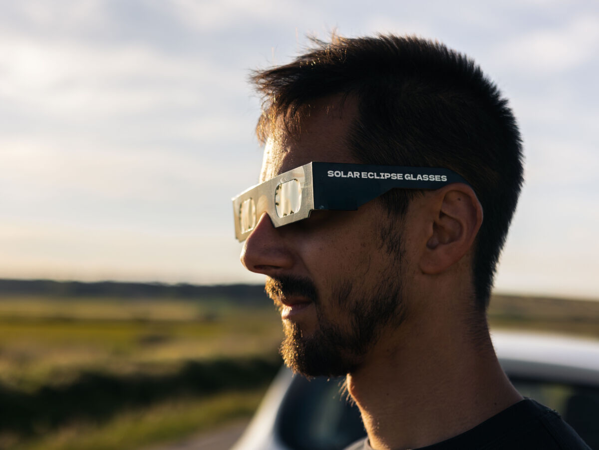 Mann mit Sonnenfinsternis-Schutzbrille aus Papier blickt in die Ferne.