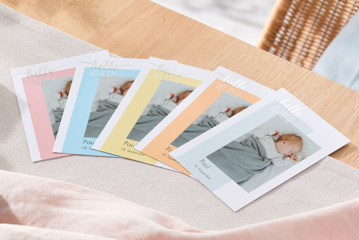Sechs individuelle CEWE Grußkarten mit Babyfotos in Pastellfarben, auf einem Tisch arrangiert.