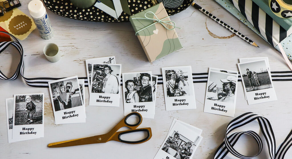DIY-Situation mit Geburtstagsfotos, Geschenk, Schere und schwarzen Schleifenbändern auf hellem Tisch