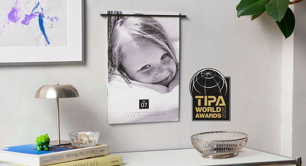 Ein schöner Kalender hängt an einer Wand. Auf einem Tisch liegen ein Lampen, Bücher und ein Korb.