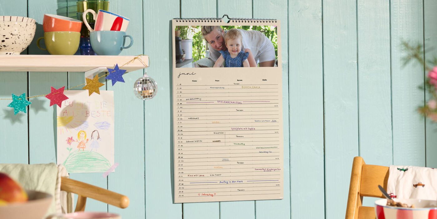 CEWE Fotokalender mit Familienfoto und handschriftlich eingetragenen Terminen an einer Küchenwand