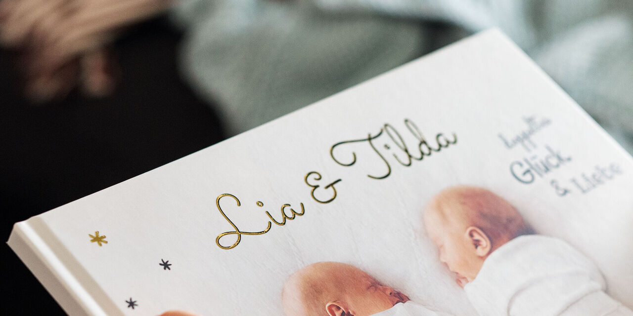 Zwei Neugeborene mit einem Fotobuch, auf dem 'Lia & Tilda' steht