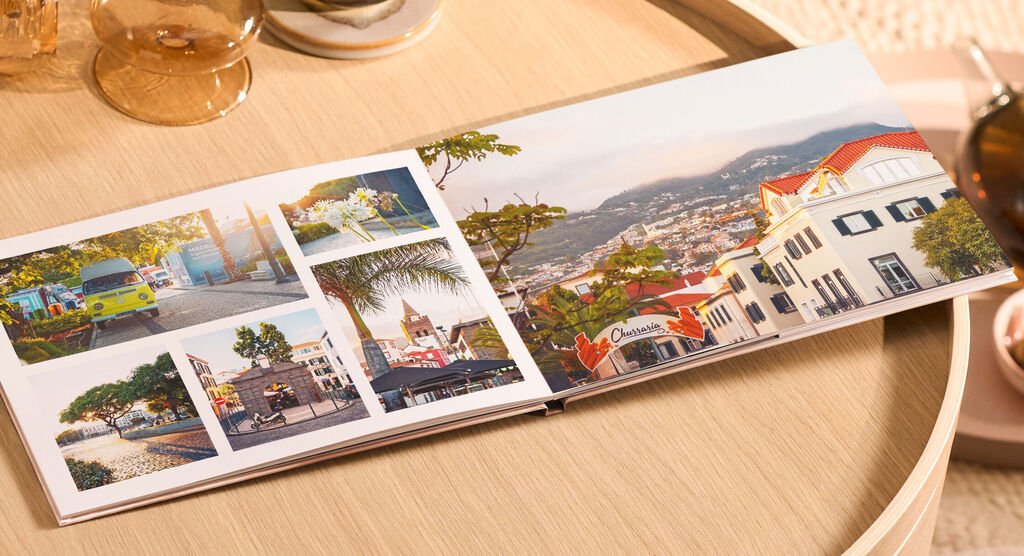 CEWE FOTOBUCH mit farbenfrohen Stadtfotos und Bergen im Hintergrund auf einem Holztisch