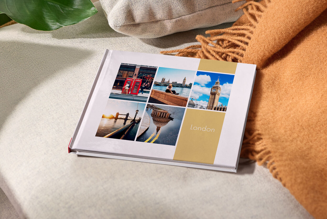 Ein CEWE FOTOBUCH mit Reisemotiven aus London liegt auf einem hellen Sofa.