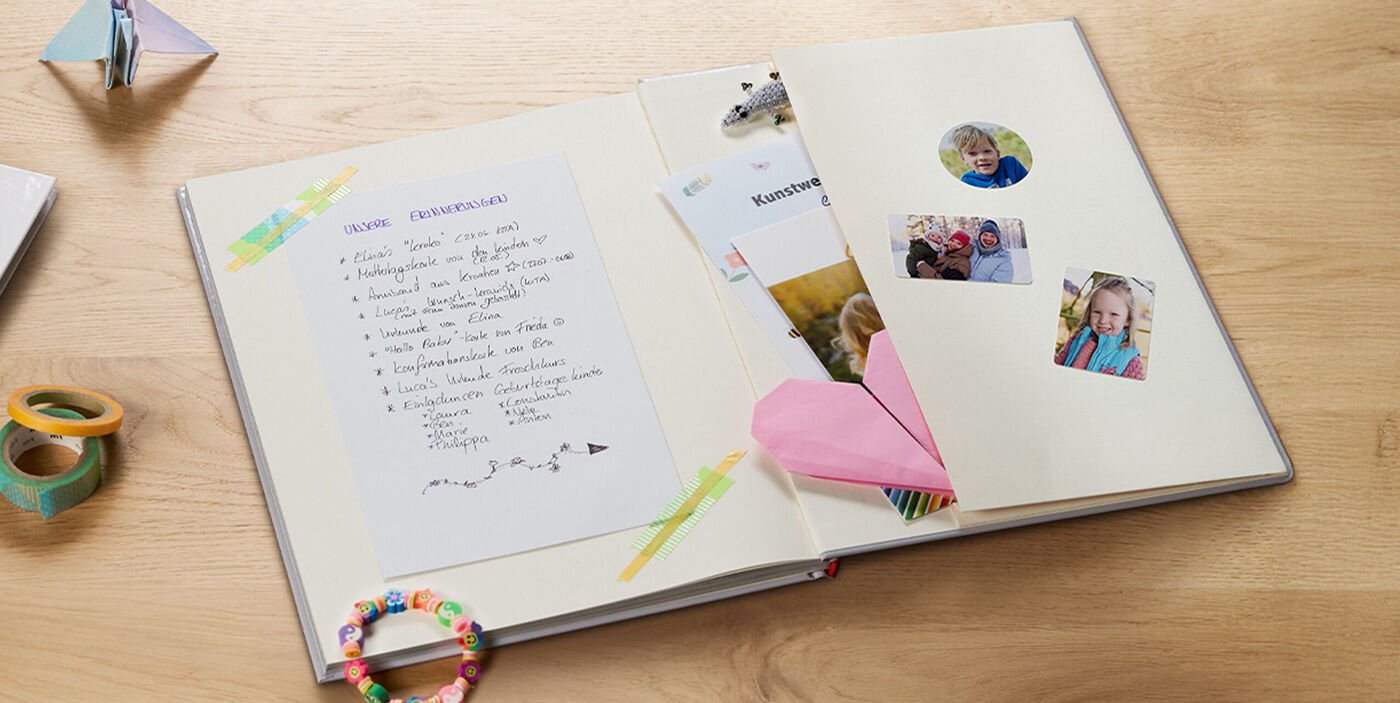 Aufgeschlagenes CEWE FOTOBUCH, auf dessen hinteren Innenseite des Einbands eine Tasche integriert ist, aus der Souvenirs rausragen