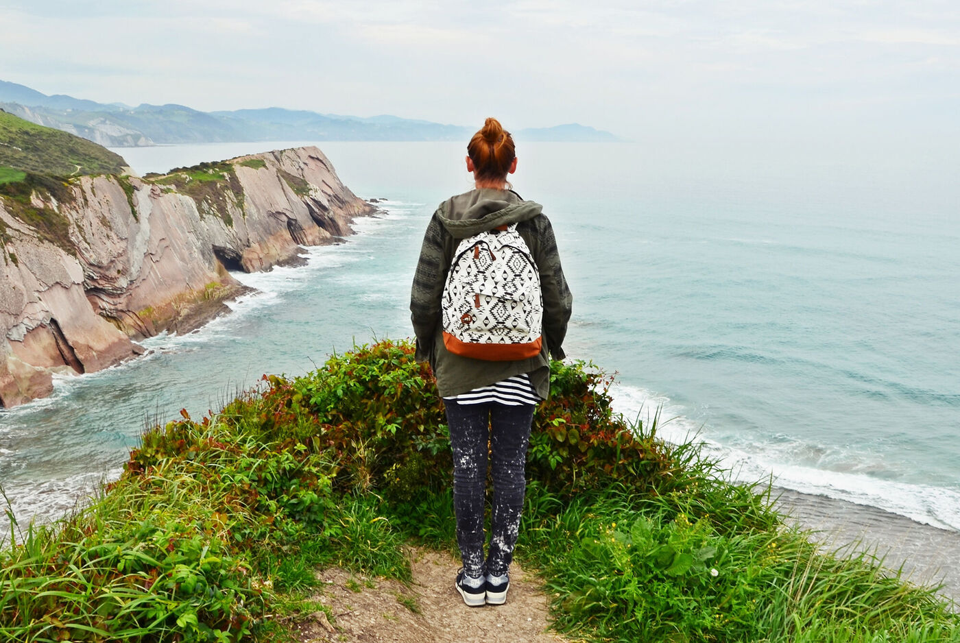 Eine Person mit Rucksack steht an einer Küste und blickt auf das Meer.