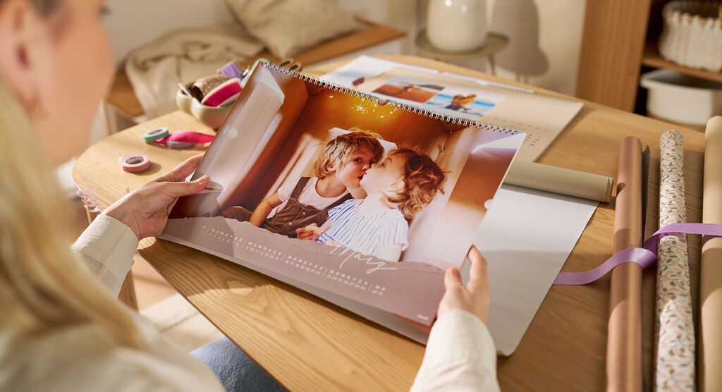 Eine Frau sitzt an einem Tisch und hält einen Wandkalender mit einem Fotomotiv von zwei Kindern in den Händen.