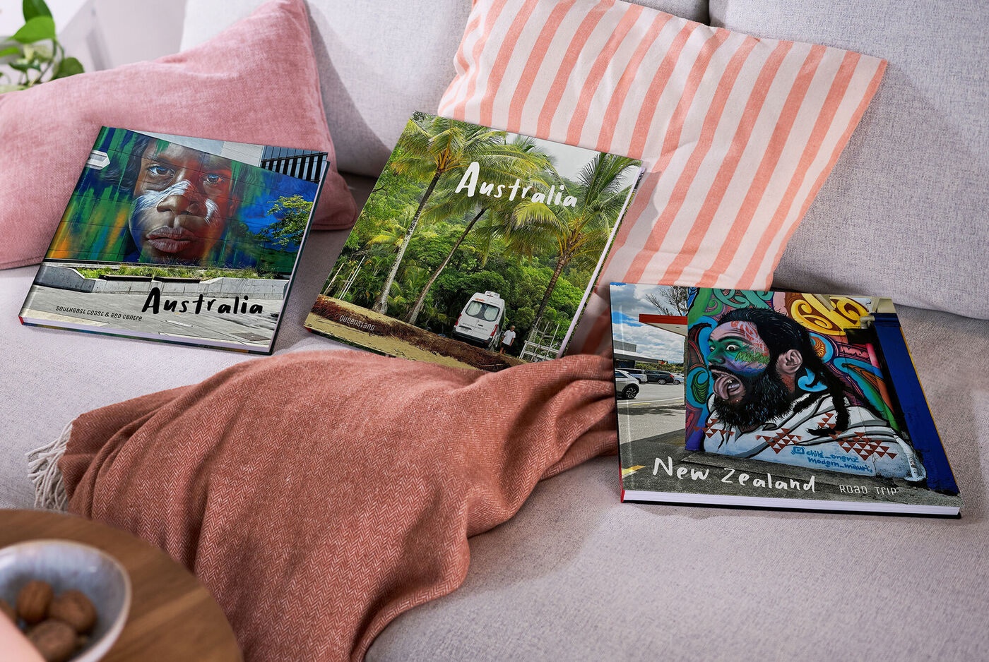 Drei Fotobücher mit Australien- und Neuseelandmotiven liegen auf einem Sofa.