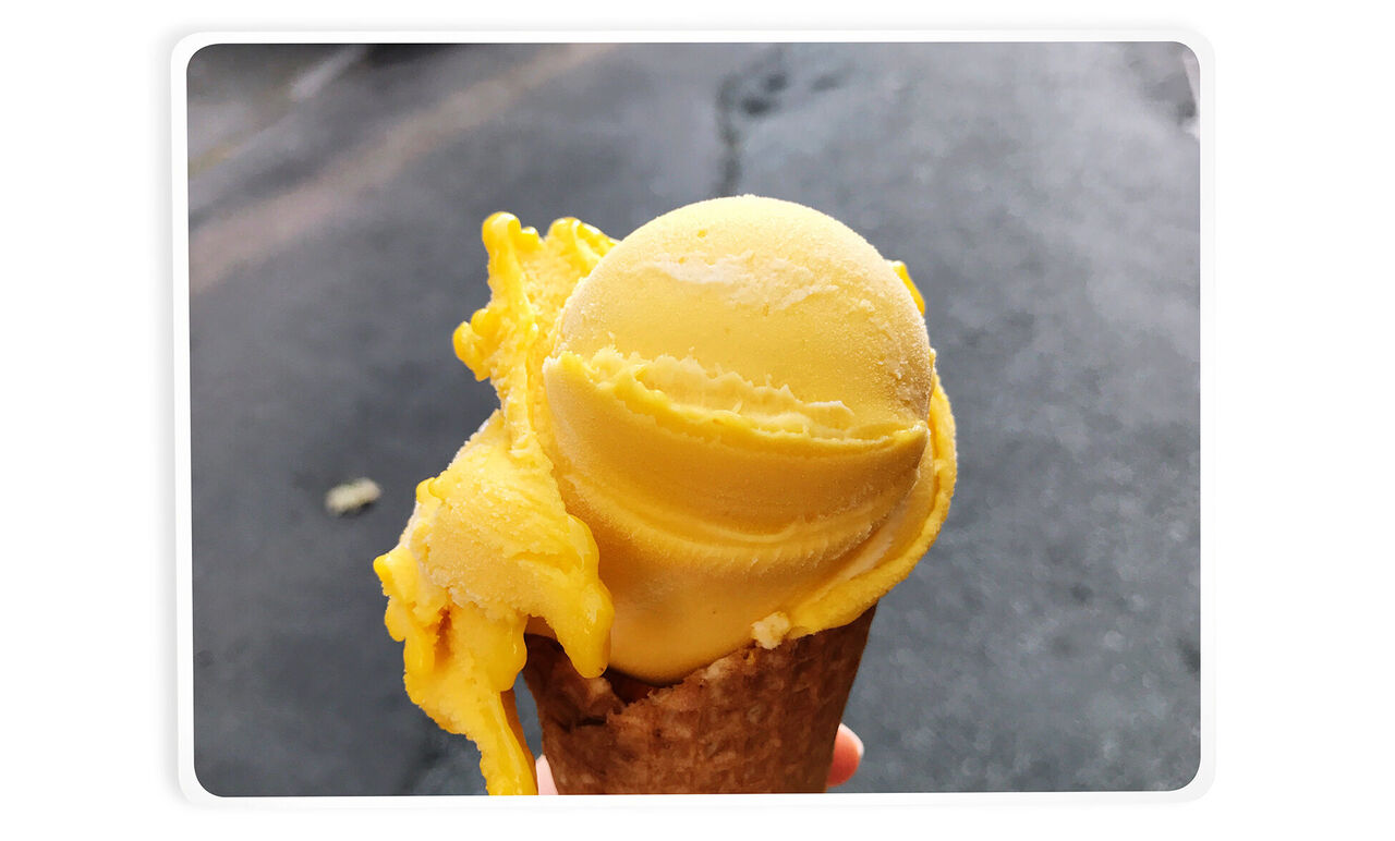 Eiskugel aus gelbem Sorbet auf einer Waffel in der Hand.