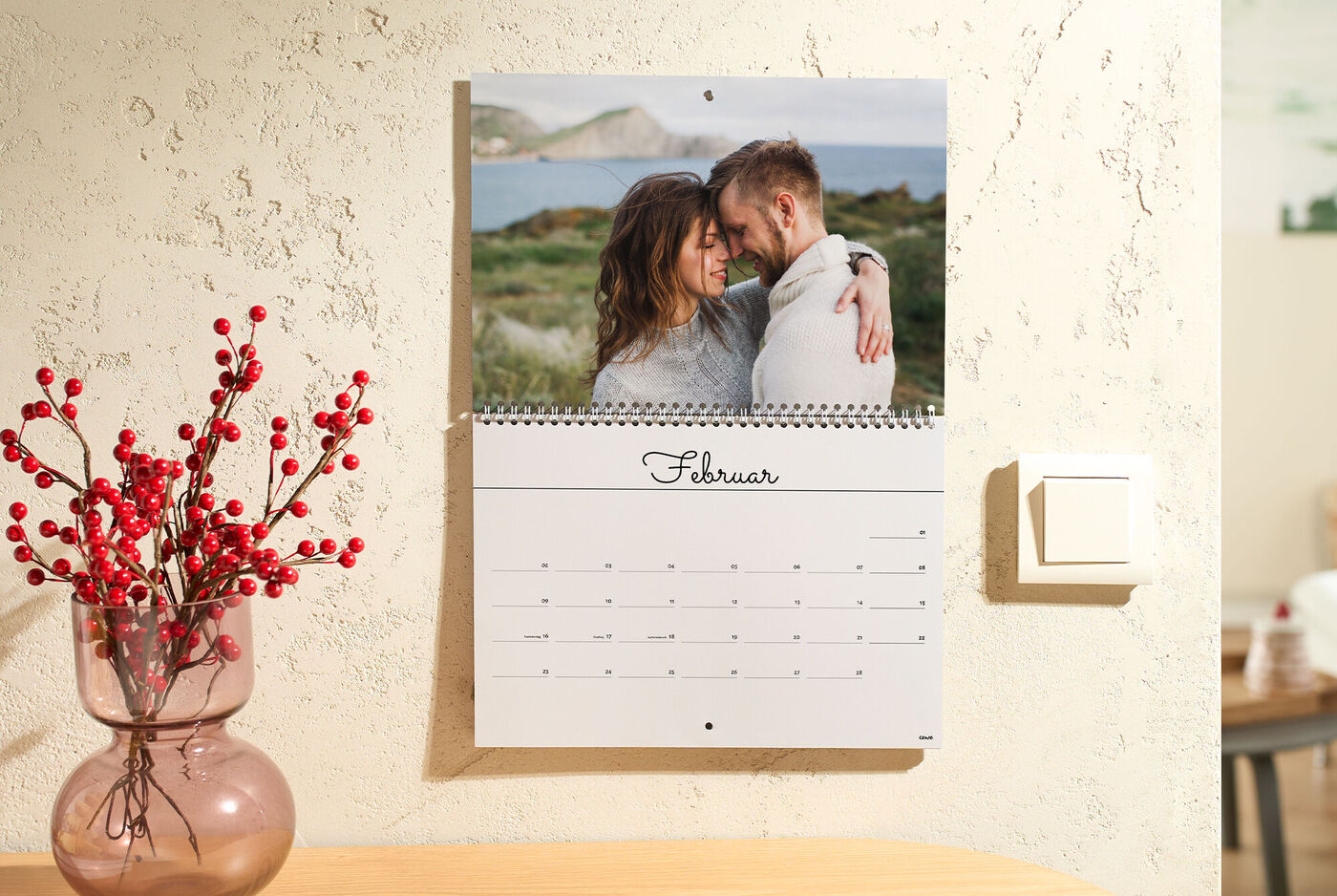 Ein CEWE Foto-Wandterminkalender zeigt auf der Februar‑Seite zwei Menschen, die sich im Freien liebevoll umarmen