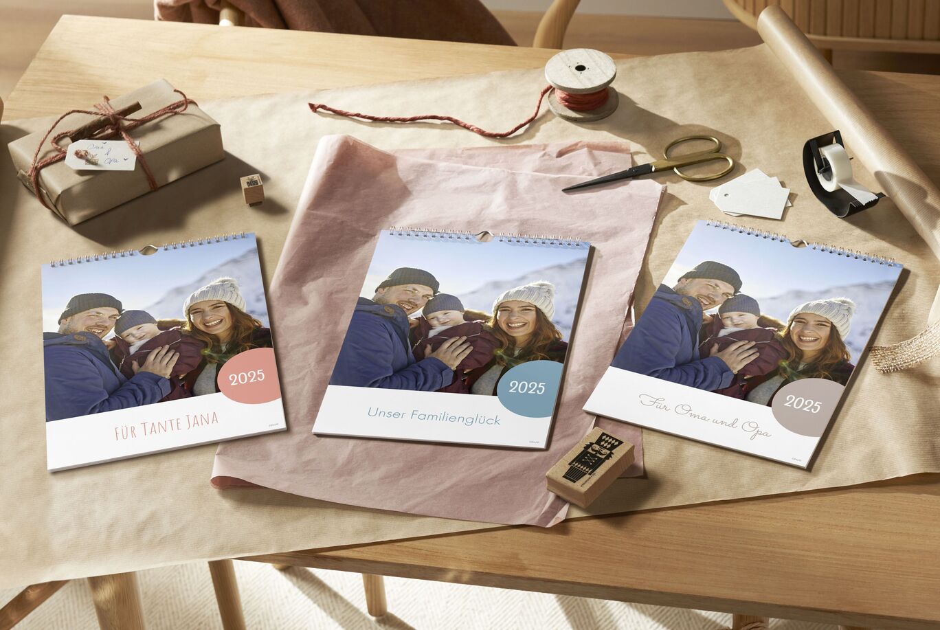Drei CEWE Fotokalender auf einem Tisch, ein Geschenk und Bastelmaterialien ringsum. Ein fröhliches Familienmoment wird festgehalten.