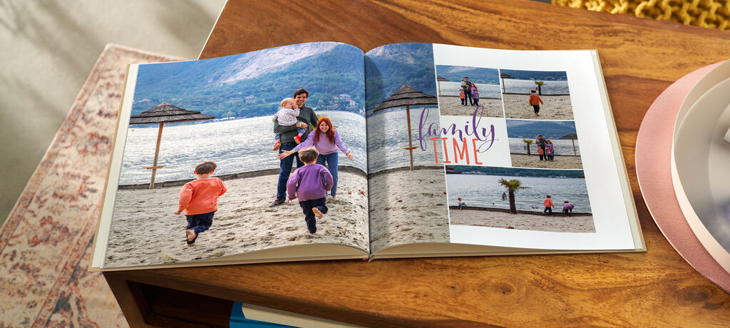 Offenes CEWE FOTOBUCH auf Holztisch mit Familienfotos am Strand und dem Text 'Family Time'