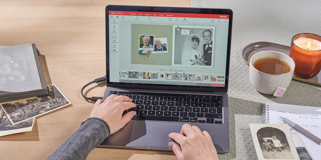 Person arbeitet an einem Laptop mit Bildern und Notizen auf dem Tisch