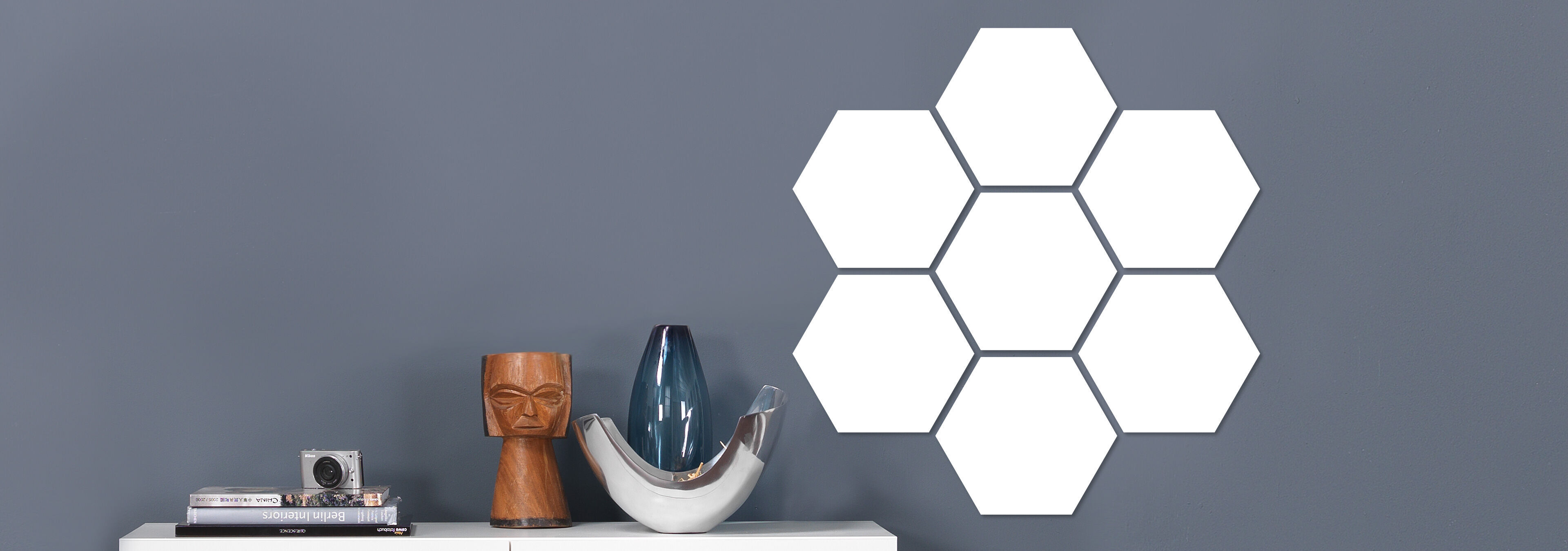 Sechs leere hexagonale Wandbilder auf grauem Hintergrund über einem Regal.