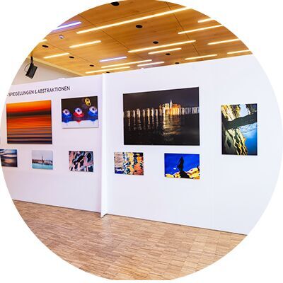 Auf einer weißen Wand sind verschiedene Fotografien in unterschiedlichen Größen befestigt.