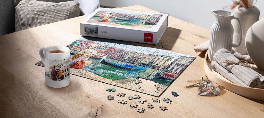 Auf einem Tisch liegen ein Puzzle und ein Schlüssel mit Fotoanhänger. Daneben steht eine Fototasse.