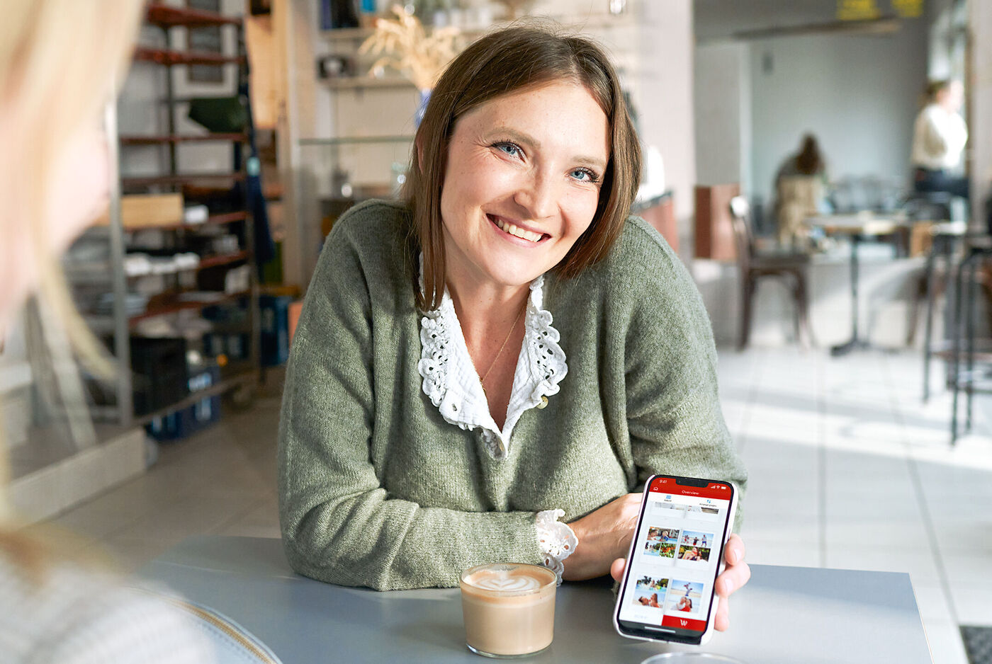 Eine Person zeigt auf ihrem Smartphone eine Auswahl an kreativen Gestaltungsideen in einem gemütlichen Café.
