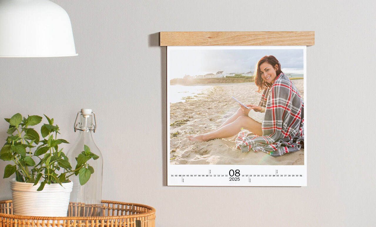 Person sitzt entspannt am Strand mit einem Buch im CEWE Fotokalender, der August 2025 darstellt