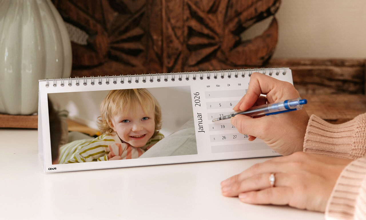 Eine Hand schreibt in einen CEWE Fotokalender für Januar 2026
