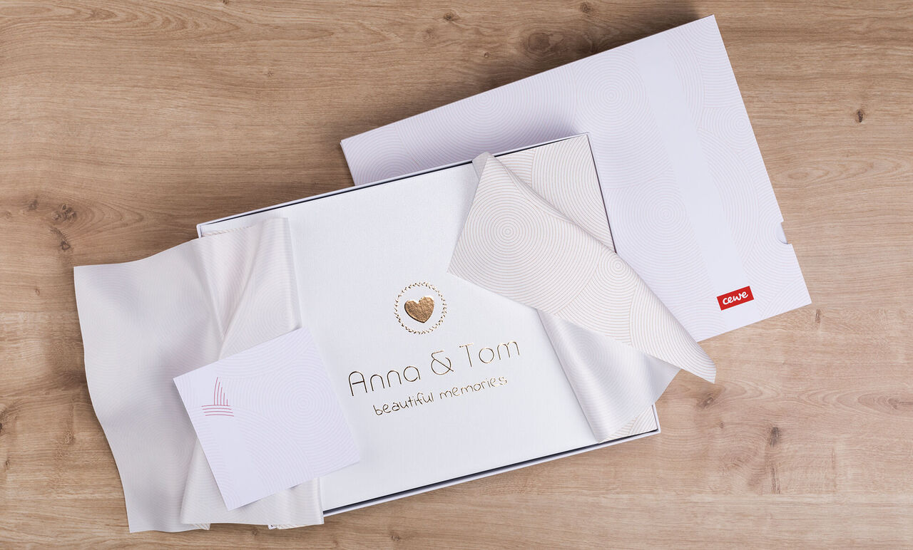 Wunderschön verpacktes CEWE Fotobuch mit einem personalisierten Cover und einer Grußkarte auf einem Holztisch.