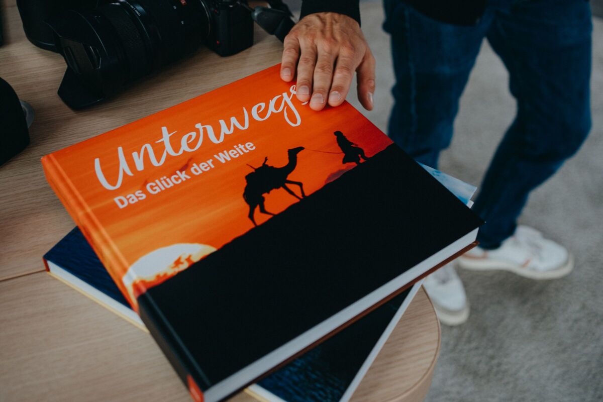 Nahaufnahme eines orangefarbenen Fotobuchs mit dem Titel „Unterwegs – Das Glück der Weite“, das auf einem Tisch liegt.