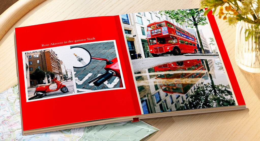 Ein offenes Fotobuch mit roten Seiten. Auf der linken Seite sind zwei Bilder von einem roten Roller und der Reflektion eines roten Busses auf der Straße. Auf der rechten Seite steht ein Bild eines roten Busses davor, der die Stadt besucht.