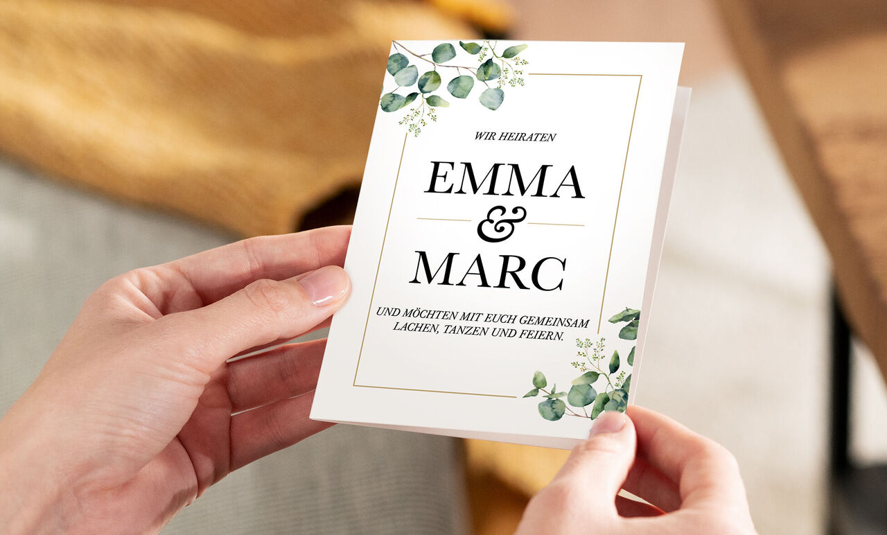 Hochzeitseinladung mit den Namen Emma und Marc, umgeben von grünen Blättern
