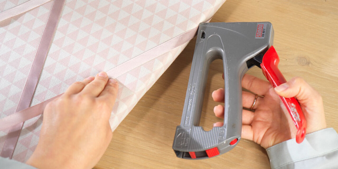 Eine Hand hält einen Handtacker, der in einen Stoffbeutel eingreift. Nutzung des Tackers für kreative Projekte.