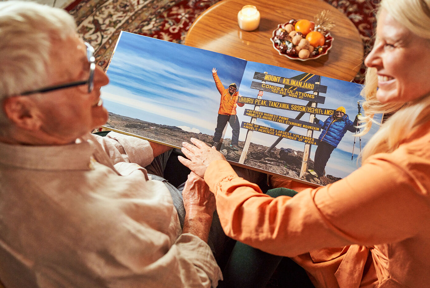 Zwei Personen betrachten zusammen ein großes Fotobuch mit Reiseerinnerungen. Das Bild zeigt eine wunderschöne Landschaft im Hintergrund.