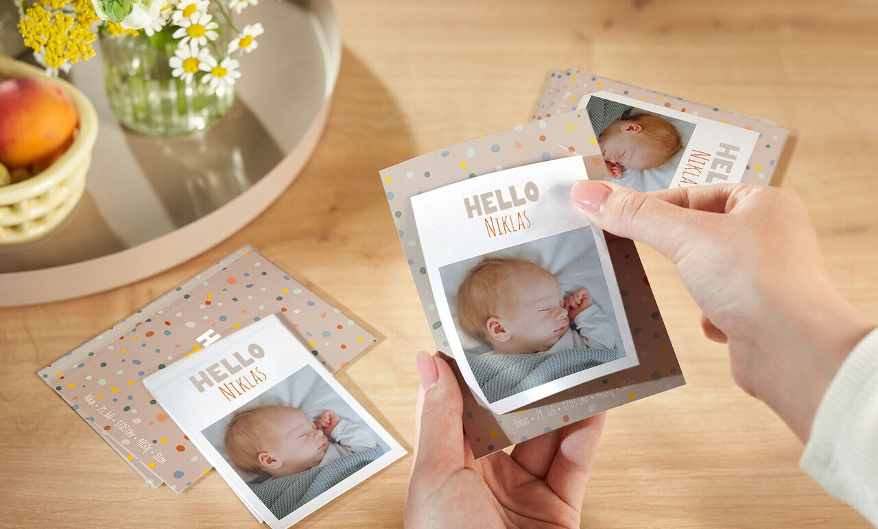 Hand hält personalisierte Grußkarten mit Babyfotos, schöne Gestaltung