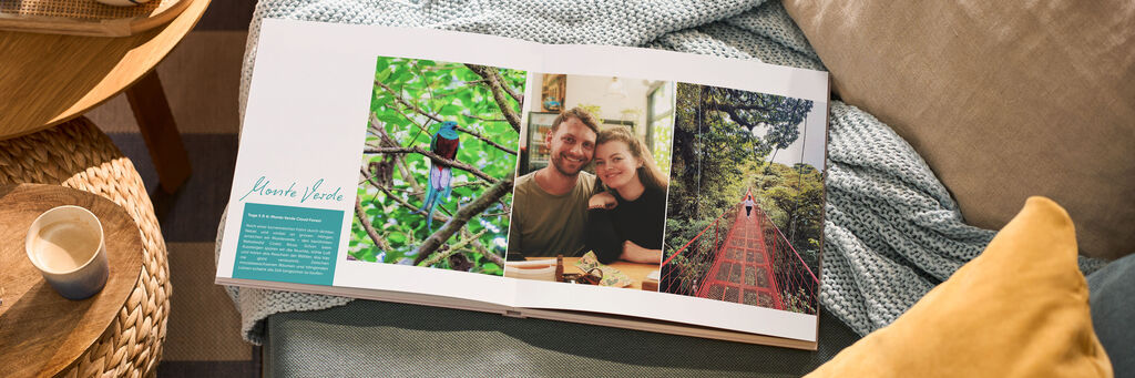 Offenes CEWE FOTOBUCH auf Sofa mit drei Fotos: Vogel im Baum, Paar lächelt, roter Steg im grünen Wald