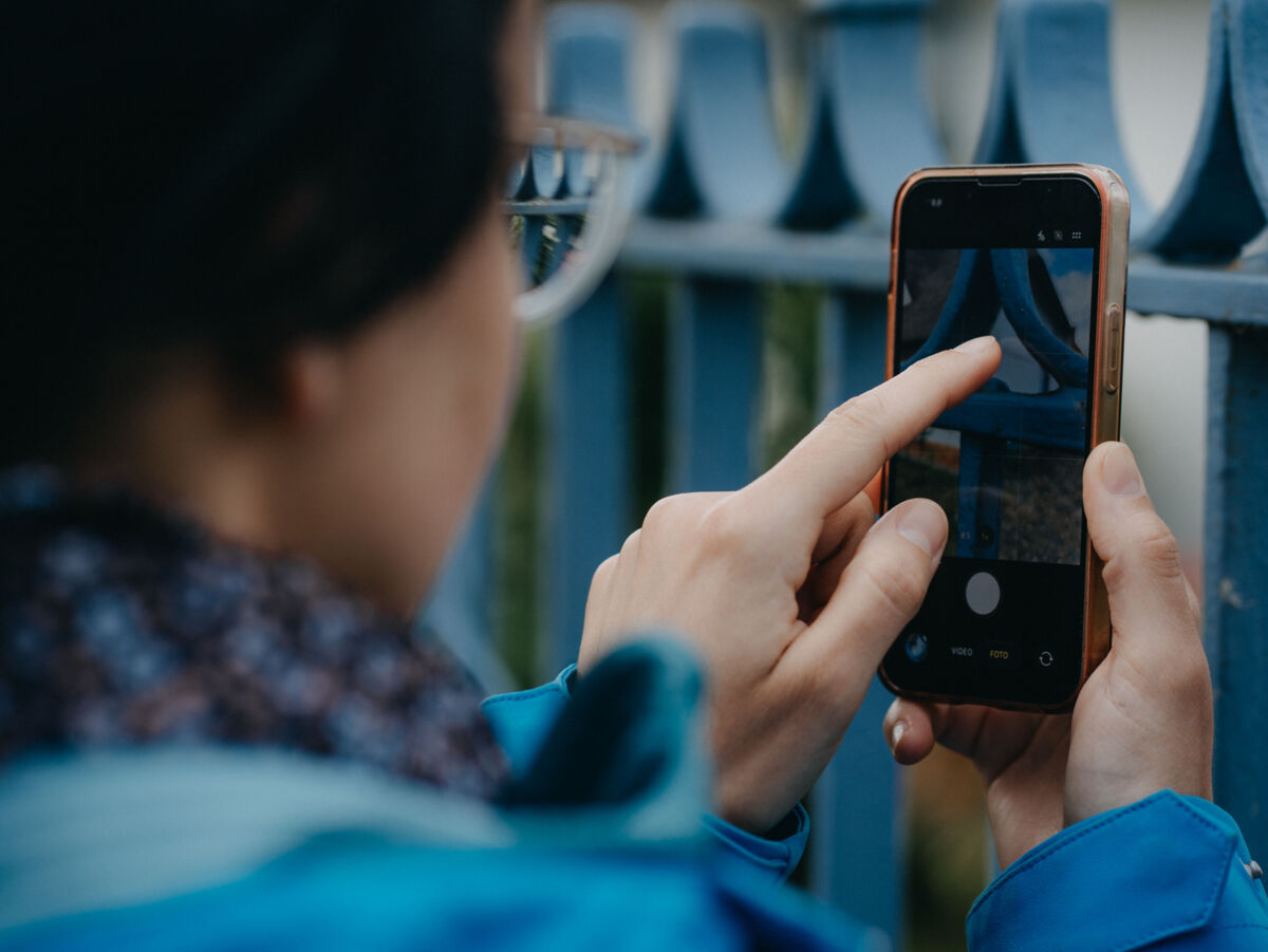 Person bedient ein Smartphone und fotografiert ein blaues Metallgitter aus der Nähe.