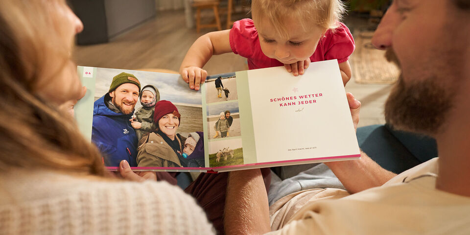 Familie blickt freudig auf ein eröffnendes Fotobuch mit bunten Urlaubsbildern.