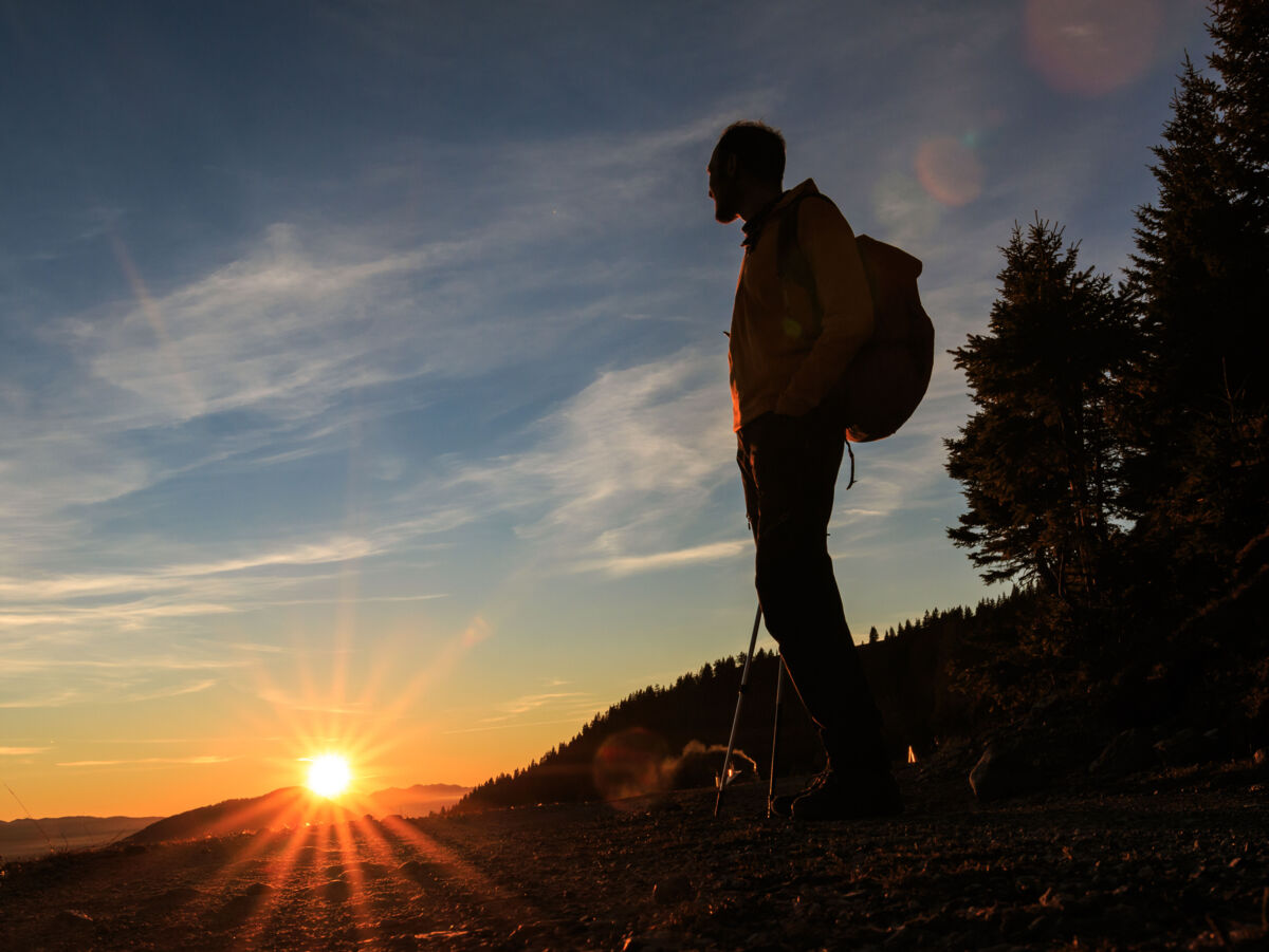 Silhouette eines Wanderers, der bei Sonnenuntergang auf einem Hügel steht