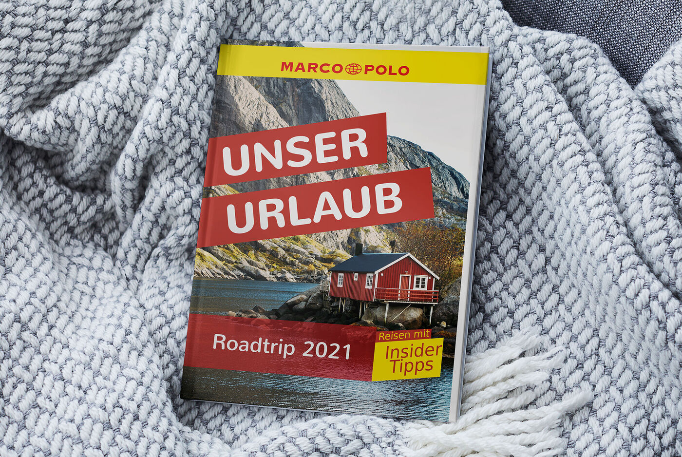 Farbenfrohes Reisefotobuch mit dem Titel 'Unser Urlaub', umgeben von einer gestreiften Decke
